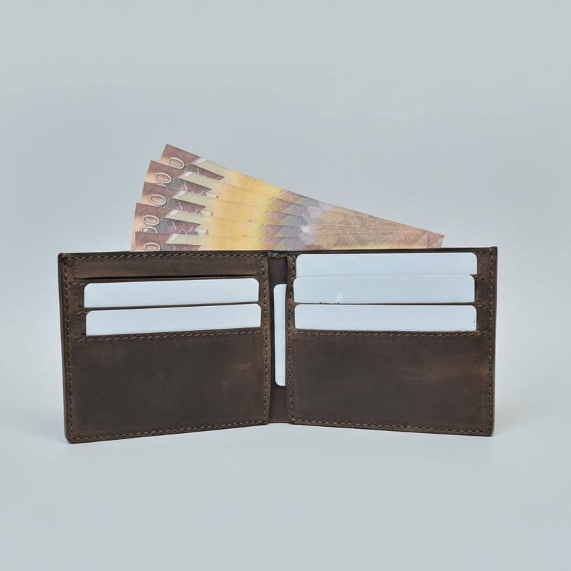 Brown leather wallet with money held by a hand on a wooden surface.