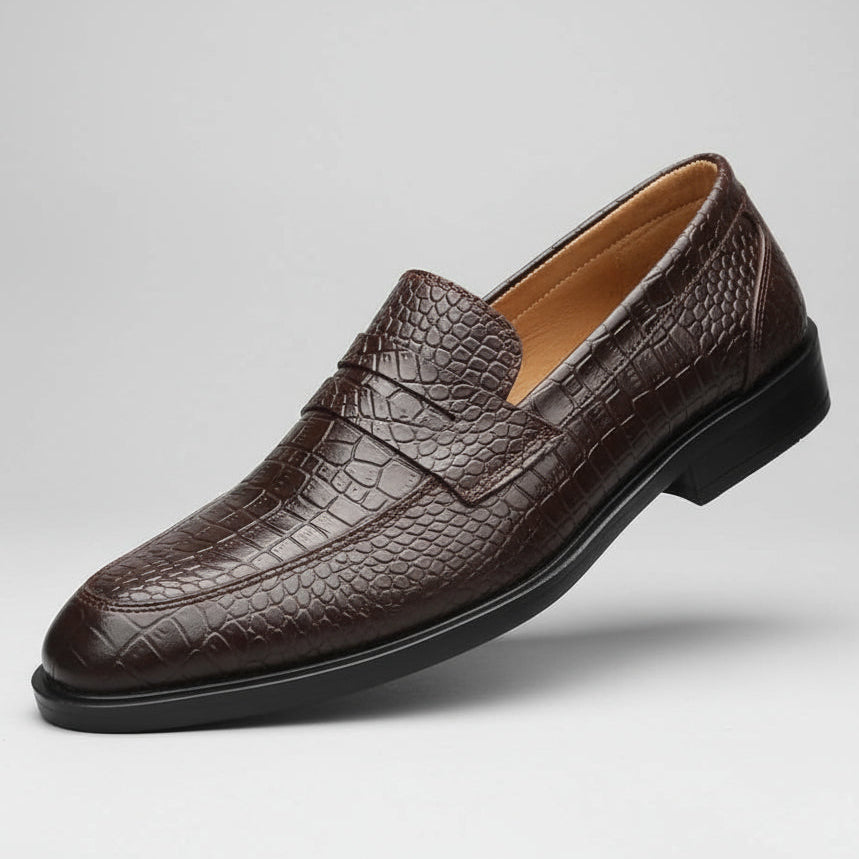 Brown leather loafer held in a hand with shoe rack in the background