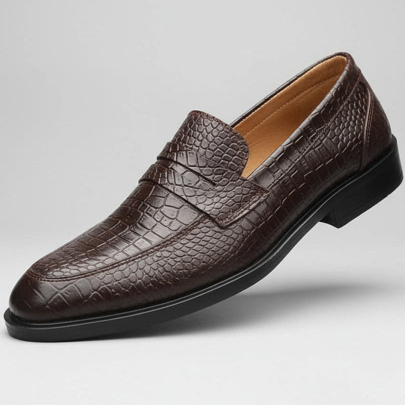 Brown leather loafer held in a hand with shoe rack in the background