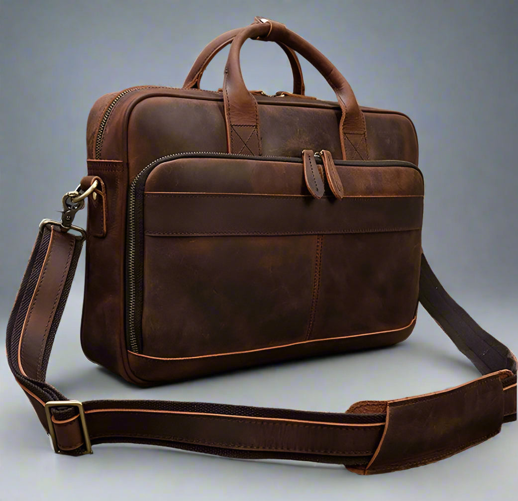 Brown leather briefcase with shoulder strap on a gray surface
