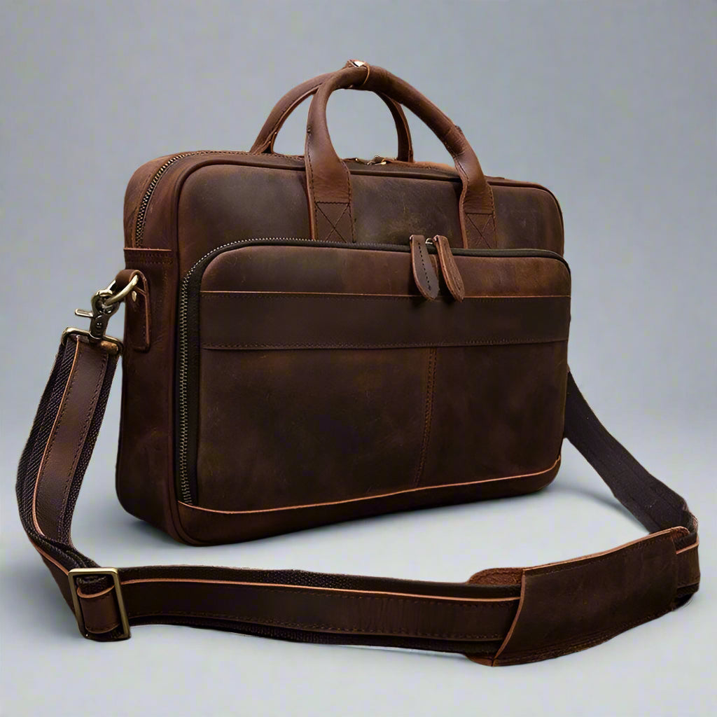 Brown leather briefcase with shoulder strap on a wooden surface