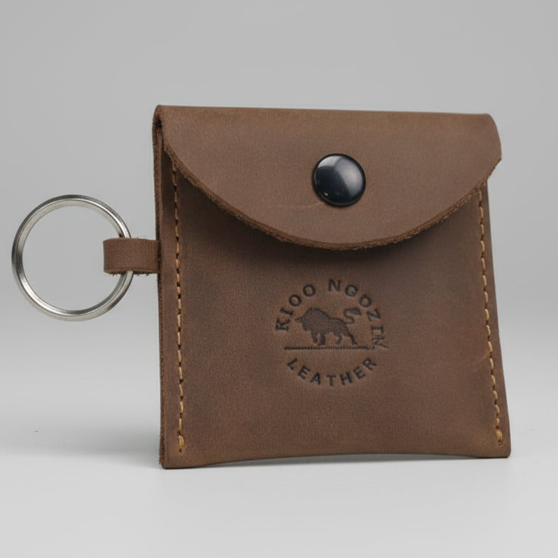 Brown leather keychain pouch with a blue button on a wooden surface