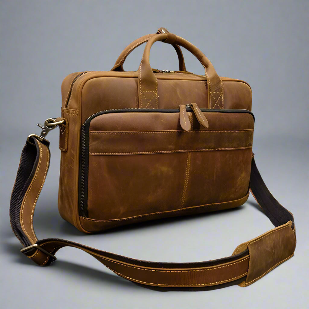 Brown leather briefcase with shoulder strap on a textured surface