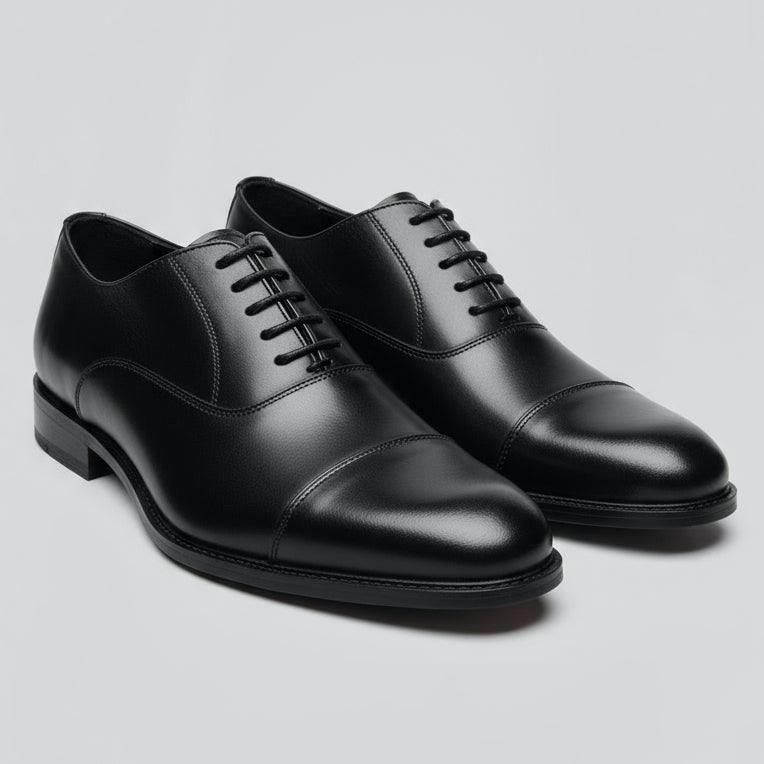 Black leather dress shoe held in a hand with a blurred indoor background