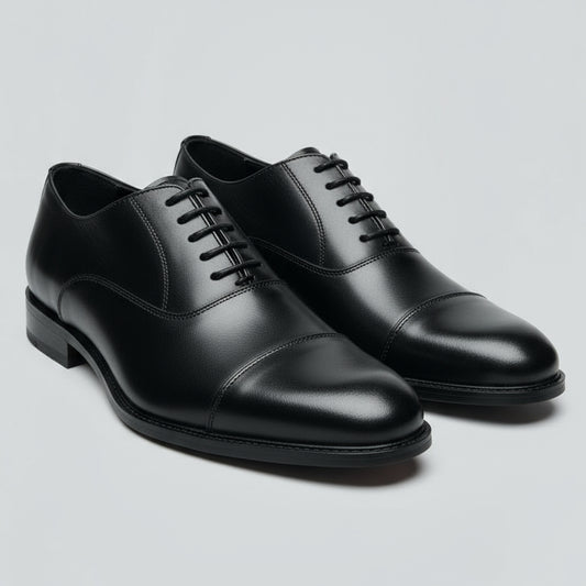 Black leather dress shoe held in a hand with a blurred indoor background