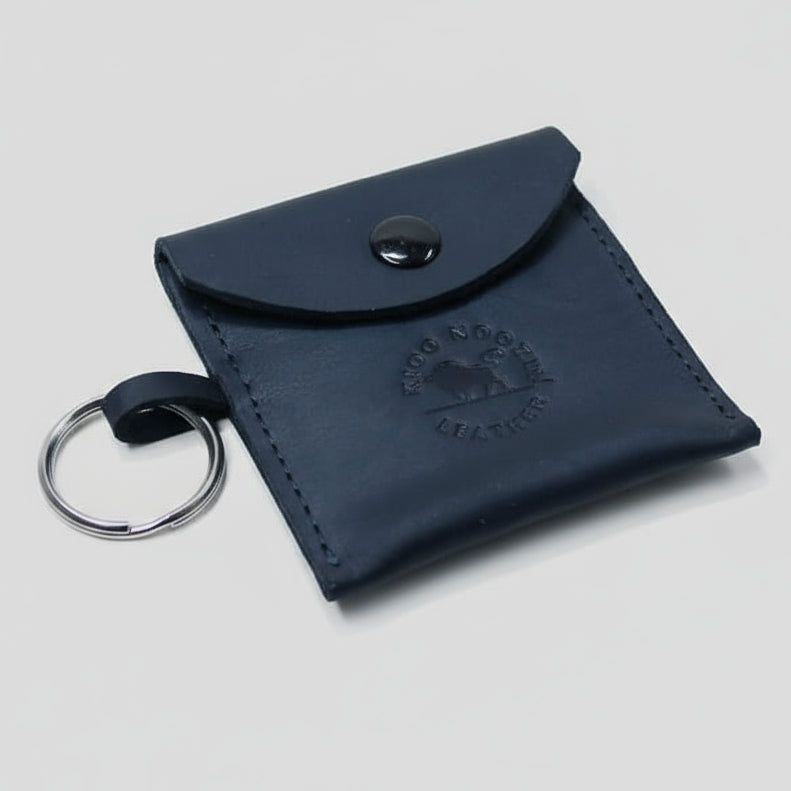 Black leather key pouch with a brand logo on a wooden surface