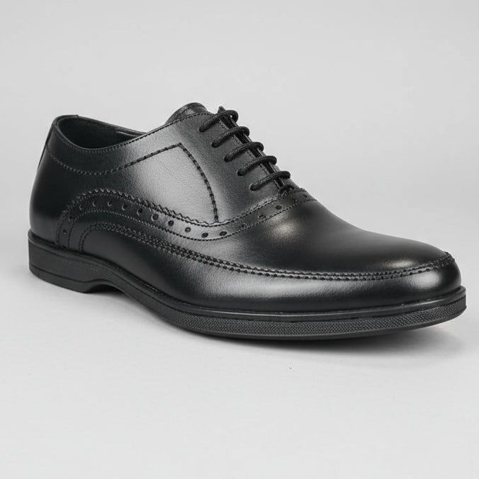 Black leather shoe with flat sole held in a hand with a blurred shoe rack in the background