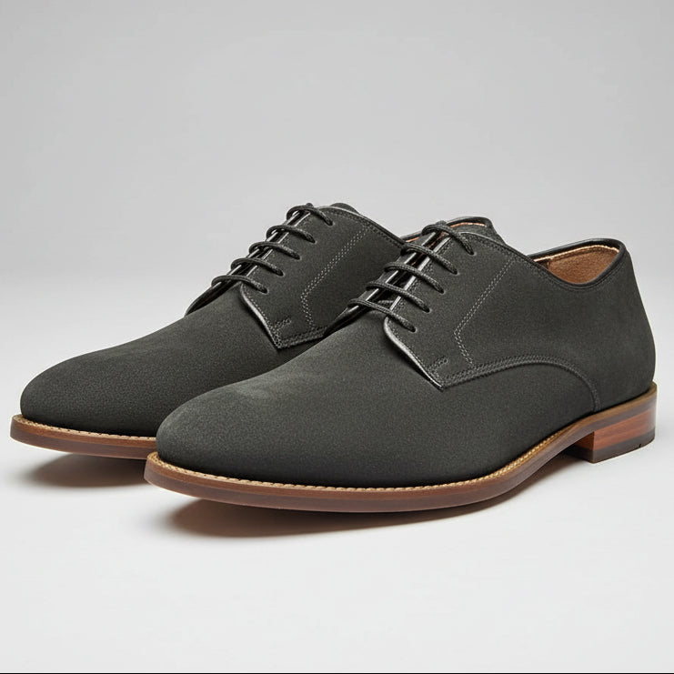 black suede shoe being held with a wooden floor and shoes in the background