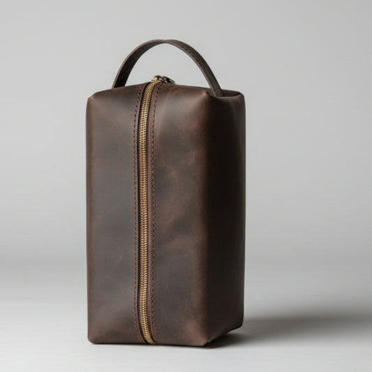 Brown leather toiletry bag with gold zipper on a light gray background