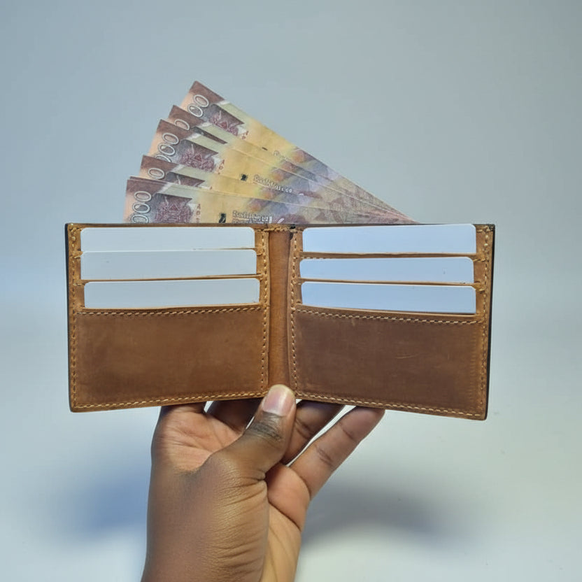 Brown leather wallet with money held by a hand against a wooden background