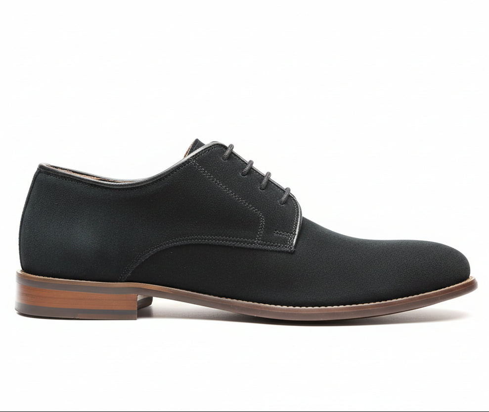 Dark suede shoe held in hand with wooden shoe rack in background