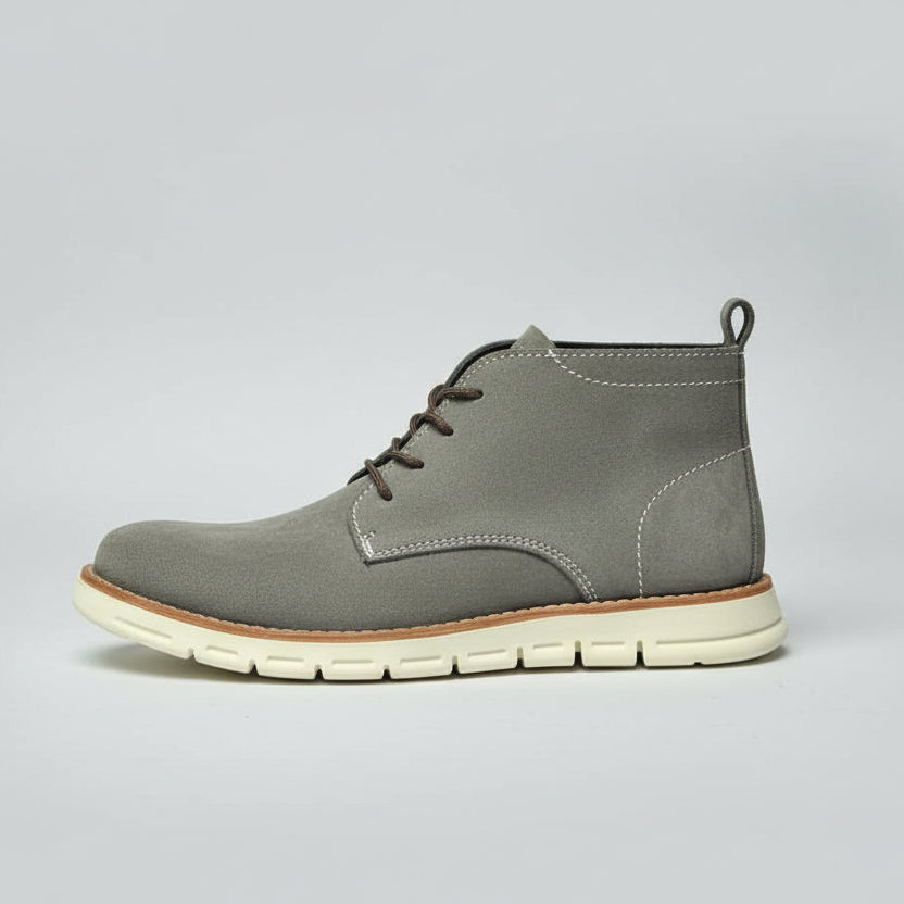 Gray suede shoe with white sole held in front of a wooden shoe rack.