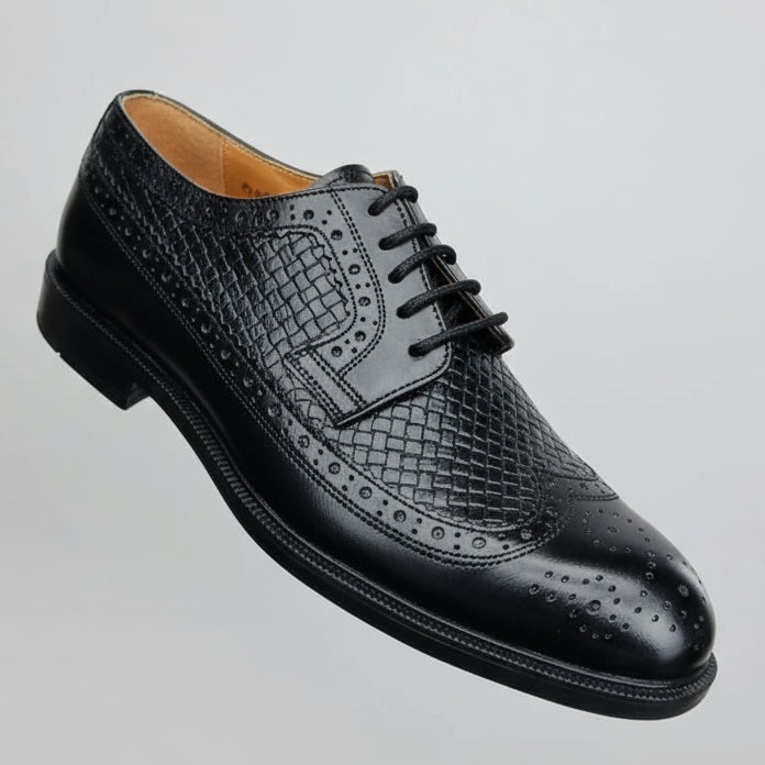 Black leather shoe held in a hand with a shoe rack in the background