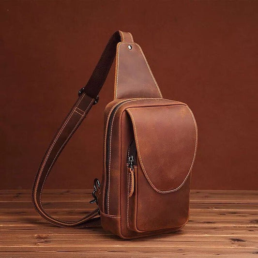 Brown leather sling bag on a wooden surface with a brown background
