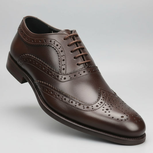 Brown leather shoe held in front of a shoe rack with various shoes.