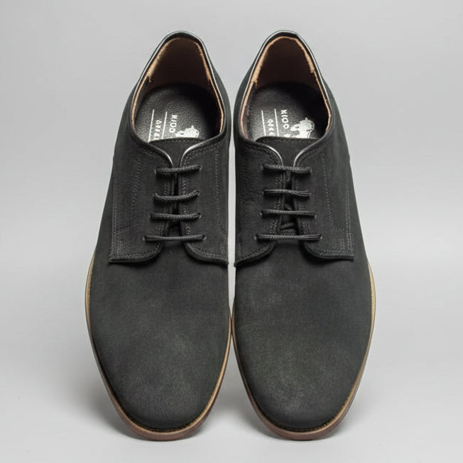 Pair of black suede shoes held up against a wooden background with other shoes.