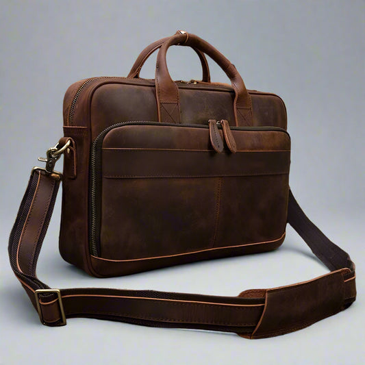 Brown leather briefcase with shoulder strap on a wooden surface