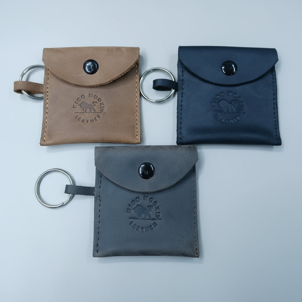 Three leather key pouches in brown, black, and gray on a wooden surface.