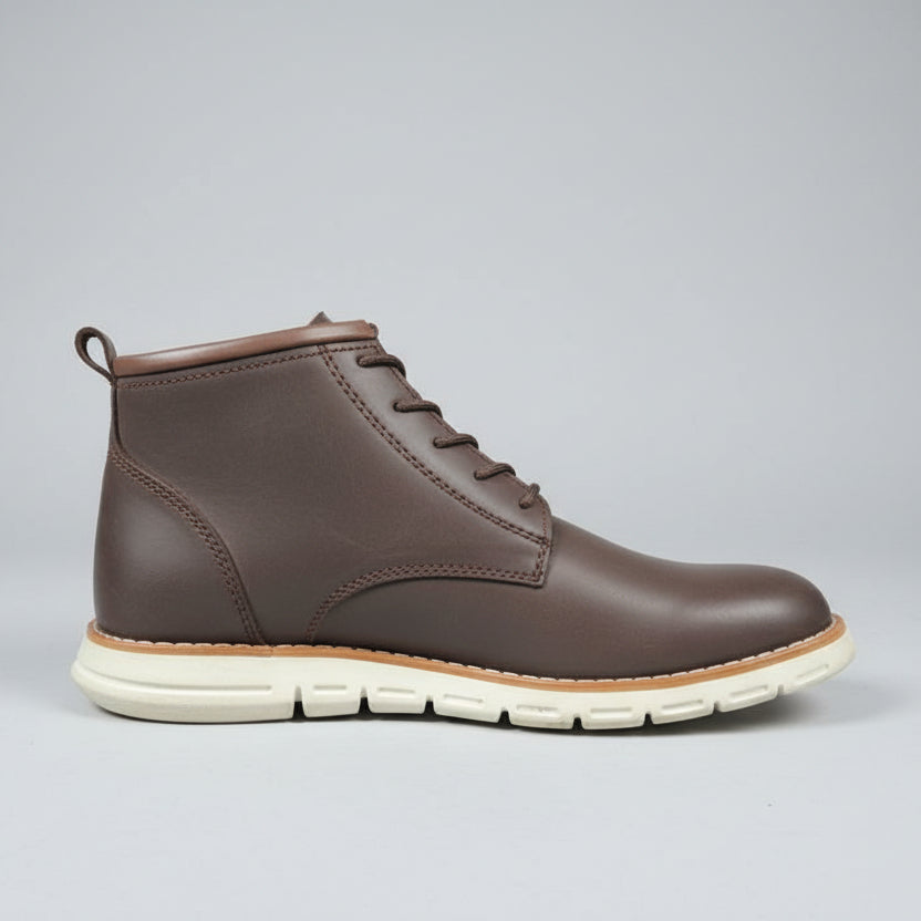 Brown leather boot held by a hand with a grid-patterned wall and shoes in boxes in the background.