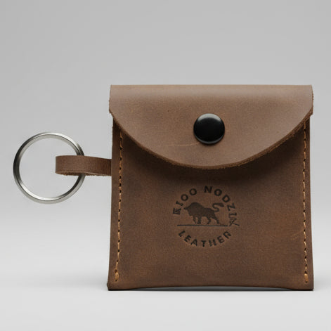 Brown leather keychain pouch with a blue button on a wooden surface