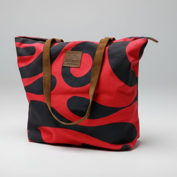 Red and black patterned bag with a brown strap on a wooden surface, with a blurred background of shelves.